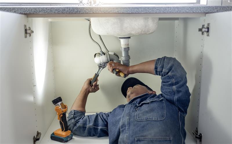 Plumber repairing pipes beneath a bathroom sink in Carlsbad