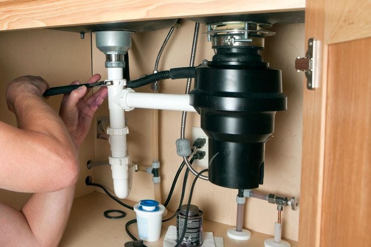 Plumber installing a garbage disposal beneath a kitchen sink in Carlsbad