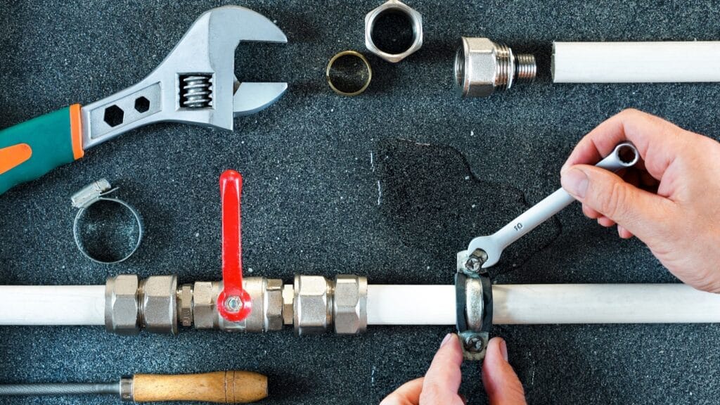 Plumber repairing a pipe valve with an adjustable wrench in Carlsbad