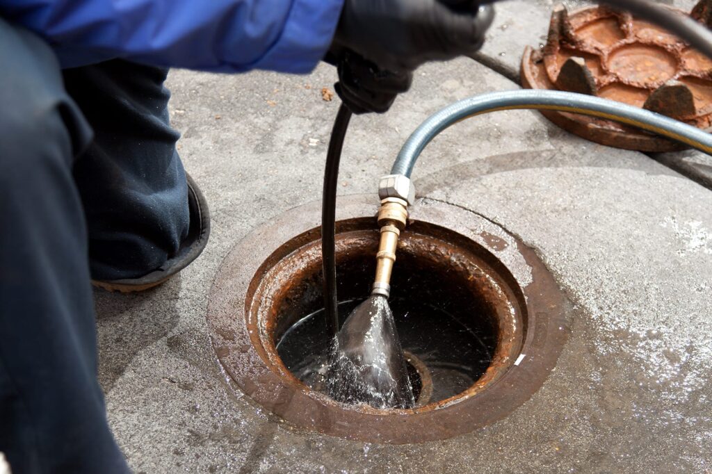 Plumber hydro jetting a sewer line through a manhole in Carlsbad