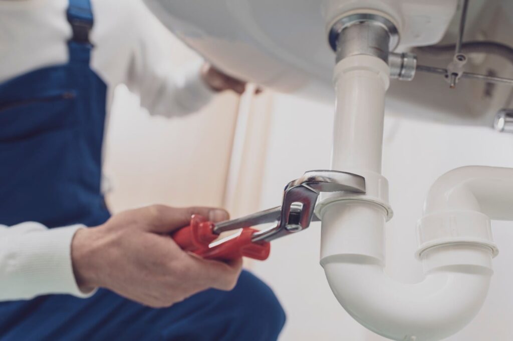 Plumber repairing a white drain pipe beneath a sink in Carlsbad