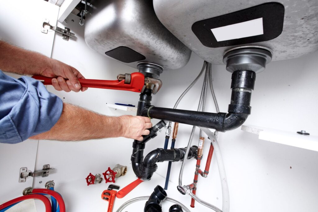 Plumber repairing drain pipes beneath a kitchen sink in Carlsbad