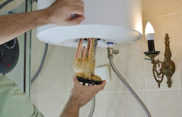 Technician removing mineral buildup from a water heater in Carlsbad